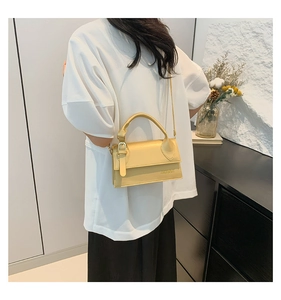 Detail of yellow faux leather crossbody bag with brand embossing and adjustable strap