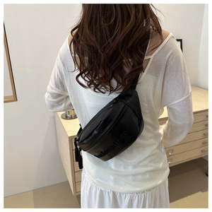 Detail of black leisure chest bag with embossed letter design and woven zipper pull