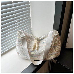 Close-up of white quilted crescent bag with wavy embroidery and wide adjustable strap