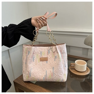 Détail d'un cabas rose en PU avec texture matelassée, broderie colorée et chaîne dorée