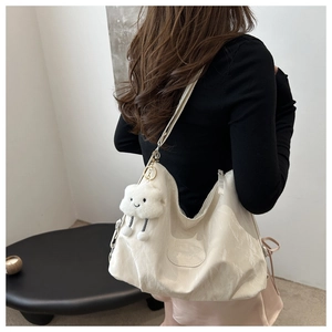 Gros plan du sac cabas beige à texture plissée et pendentif nuage porté par un mannequin