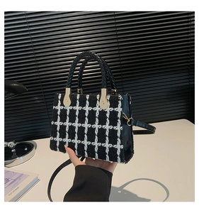 Detail of black and white tweed crossbody bag with gold hardware and woven handles