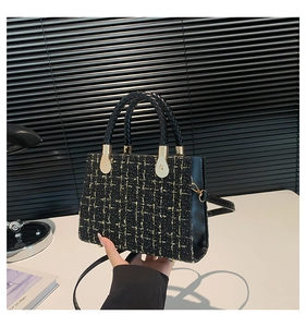Detail of black tweed handbag texture with gold metallic accents and leather handle