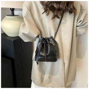 Detail shot of a black drawstring bucket bag with heart patch and long crossbody strap