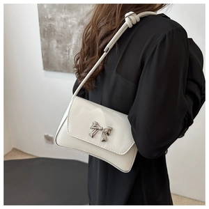 Gros plan sur le sac à bandoulière en cuir verni blanc avec nœud argenté et sangle nouée