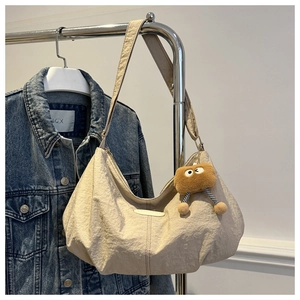 Detail of off-white pleated crescent bag with a cute brown plush charm on a hanger