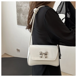 Détail du sac à bandoulière en cuir blanc brillant avec nœud argenté et sangle nouée