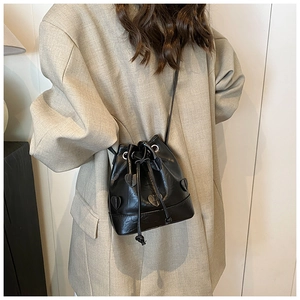 Detail of black drawstring bucket bag with heart applique worn with beige blazer