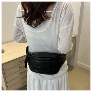 Detail of black leather crossbody bag with embossed logo and zipper closure on a model
