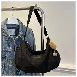 Detail view of black crescent shoulder bag with silver buckle and plush ball charm