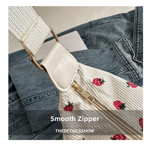 Detail of smooth gold zipper and red strawberry print on white corduroy bag fabric