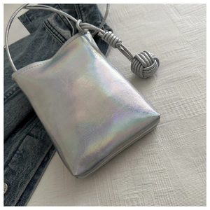 Détail du sac bandoulière holographique argenté avec bandoulière tressée nouée sur denim