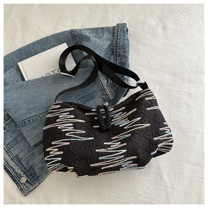 Detail of black textured canvas bag featuring colorful zigzag embroidery and knotted zipper pull