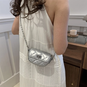 Mini sac argenté à matelassage losange porté par un mannequin en robe d'été blanche