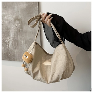 Detail of beige pleated nylon crescent bag with leather fashion patch and plush charm