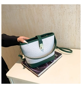 Close-up of quilted white leather bucket bag with green trim and gold metal clasp detail