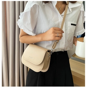 Detail of a beige faux leather saddle bag with embossed logo and metal buckle