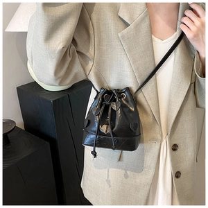 Detail of black drawstring bucket bag featuring heart patches and glossy textured finish