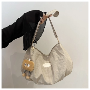 Detail of beige crescent tote bag featuring pleated texture and cute plush pendant
