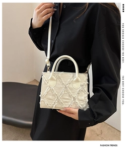 Detail showing white fabric crossbody bag with diamond quilted pattern and fringe edges