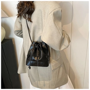 Detail of black drawstring bucket bag with pleated PU leather and heart charm worn by model