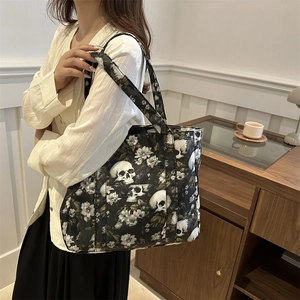 Stylish black tote bag with skull and floral prints shown on shoulder in a cozy interior