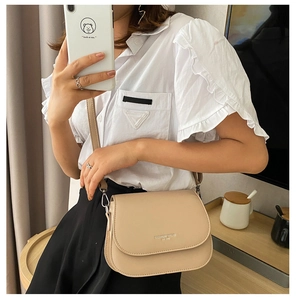 Model wearing a minimalist beige leather saddle bag with shoulder strap and silver hardware
