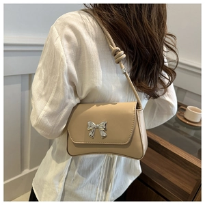 Détail d'un petit sac beige avec boucle en forme de nœud argenté et fine bandoulière