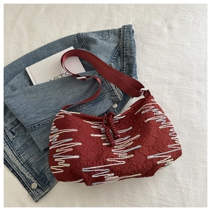 Detail of burgundy quilted canvas bag with colorful wavy embroidery and nylon strap