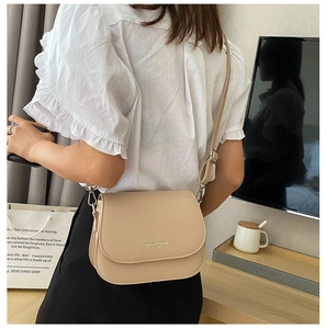 Chic beige saddle bag with adjustable strap and metallic logo shown in a lifestyle setting