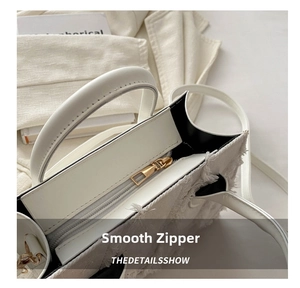 Detailed close-up of smooth gold zipper and white leather trim on frayed canvas handbag