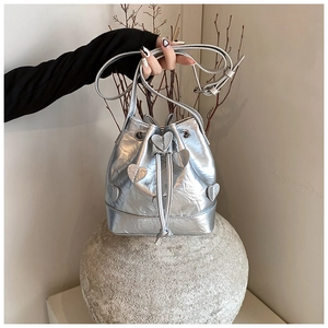 Close-up of silver pleated bucket bag with metallic heart charms on a stone base