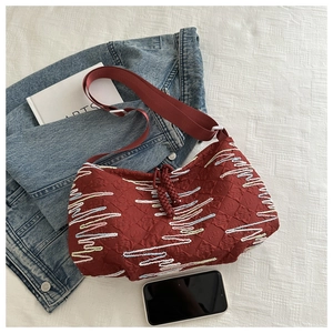 Close-up of deep red striped embroidered crossbody bag with woven strap and charms