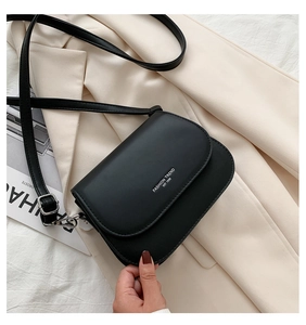 Detail view of black leather saddle bag with fashion typography on a beige blazer