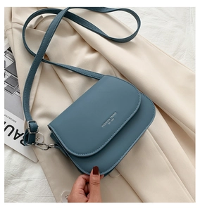 Detailed view of blue matte saddle bag on a beige blazer with fashion magazine