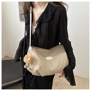 Detail of beige pleated crossbody bag featuring a plush charm and fashion plaque