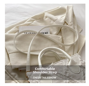 Detail of white denim crossbody bag with textured fringe edges and gold-tone hardware