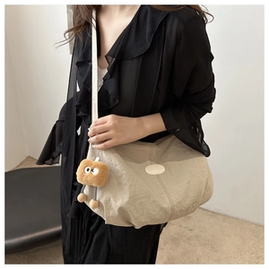 Detail of beige textured shoulder bag with fashion logo and plush charm worn by model