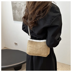 Detail of hand-woven straw crossbody bag with white leather trim worn by model