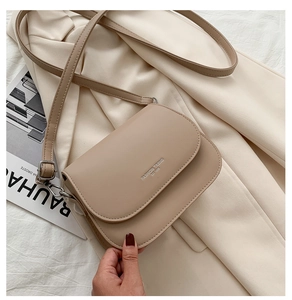Detail of a beige minimalist saddle bag with metal logo and adjustable shoulder strap