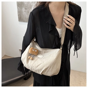 Detail of light beige pleated shoulder bag with fashion leather tag and plush charm