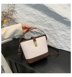 Detail of minimalist white woven bucket bag with brown leather trim and gold lock