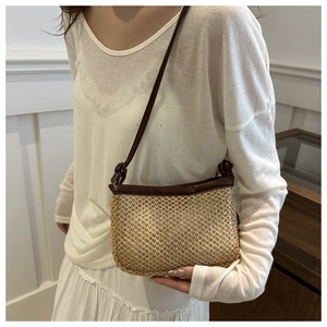 Detail of woven straw crossbody bag with brown leather straps worn by a model