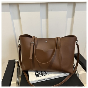 Close-up of brown leather tote bag with metal buckle on a chair and book
