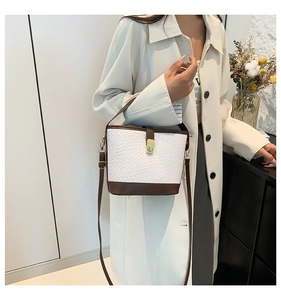 Detail of white woven bucket bag with brown leather trim and golden twist lock closure