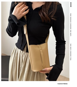 Detailed shot of beige lychee leather crossbody bag with buckle and model wearing a black top