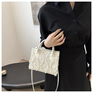 Detail of cream tassel fringed tote showing textured fabric and dual top handles