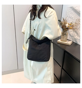Detail of a black large-capacity tote bag with a woven strap on a model in a trench coat