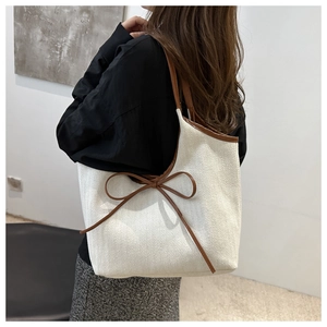 Detail of white canvas tote bag with brown faux leather trim and ribbon bow on model