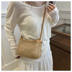 Detail of woven straw crossbody bag with brown leather trim and slim shoulder strap
